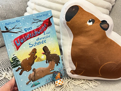 Abbildung der Gewinnspielpreise: Das Kinderbuch Drei Wasserschweine & der allererste Schnee von dtv sowie weitere Preise von Nici: ein Capybara-Kissen und eine Schneekugel.